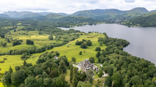 An aerial view of Wray Castle, and the side of Wray Castle House to its left, showing the field beyond the cottage, leading up to Lake Windermere, Cumbria